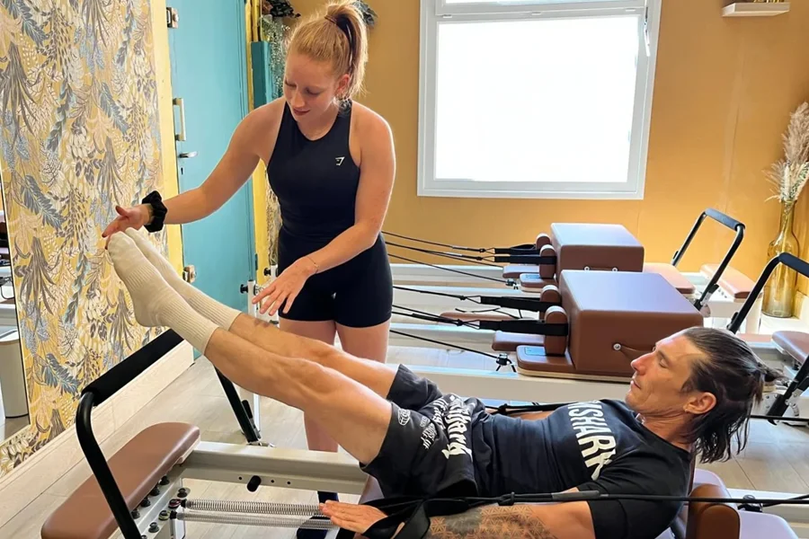 Coach accompagnant un pratiquant pendant un exercice de Pilates Reformer au Club Europole à Grenoble.